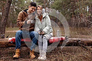 Happy couple with hot drinks spending time together in forest