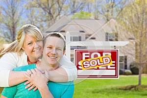 Happy Couple Hug In Front of Sold Real Estate Sign and New House