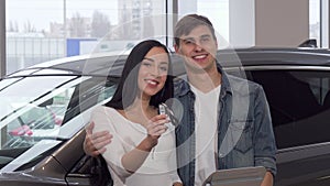Happy couple hugging, holding car keys at dealership salon