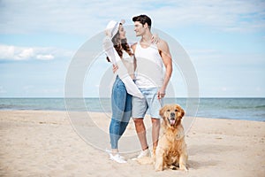 Happy couple hugging while walking with dog on the beach