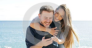 Happy couple joking and using phone on the beach