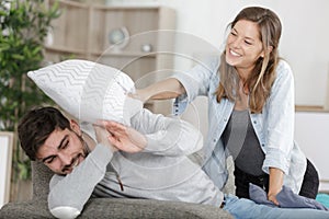 Happy couple jokingly holds pillow fight on sofa