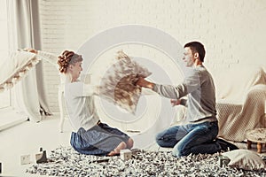 Happy couple jokingly holds the pillow fight on the sofa in the living room