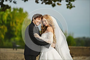 Happy couple of just married, fashionable young blonde woman in the wedding dress hugs with the stylish handsome young