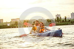 Happy couple kayaking on river with sunset on the background