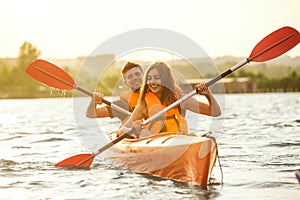 Happy couple kayaking on river with sunset on the background