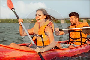 Happy couple kayaking on river with sunset on the background