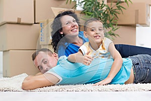 Happy couple with a kid in their new home laying on the floor