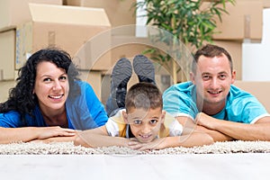 Happy couple with a kid in their new home laying on the floor wi