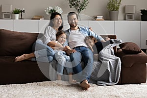 Happy couple and kids sit on sofa look at camera