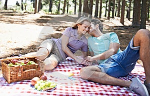 Happy couple, kiss and relax in nature for picnic, love or support in affection, date or outdoor bonding. Woman and man