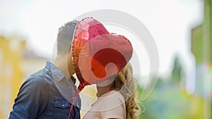 Happy couple kissing, hiding behind heart balloon, romantic relationship, date photo