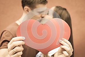 Happy couple kissing and holding heart at red wall background