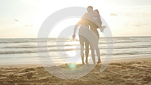 Happy couple kissing and hugging each other at the sea beach at sunset. Young man and woman in love having fun together