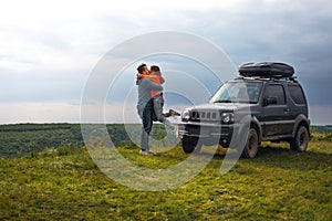 Happy couple kissing and hugging standing on the top of the mountain. Car trip on SUV with roof rack, trip at summer day. Man and