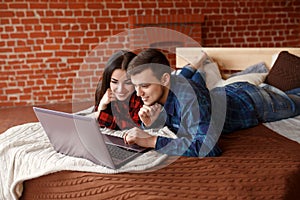 Happy couple with laptop spending time together at home, browsing internet in bed, smiling and having fun