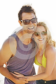 Happy, couple and laugh on vacation by beach with sunglasses, hug and holiday for memories or honeymoon. Woman, man and