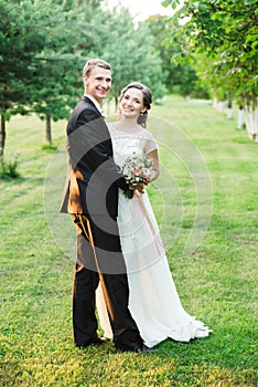 Happy couple laughing happily while cuddling each other on their wedding day in a green garden