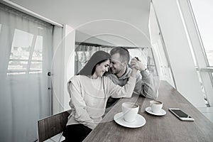 Happy couple laughing and holding hands looking at each other. Bi white room with panoramic windows. Young man and woman