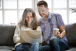 Happy couple laughing looking on laptop screen sitting on sofa