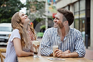 Happy couple laughing while sitting at sidewalk cafe