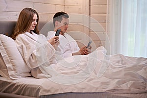 Happy couple laying in bed and looking at smartphones screens