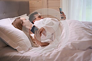 Happy couple laying in bed with phones in hands