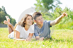 Happy couple lie on grass point with hand to something