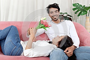 Happy couple in living room, woman lying on the lap of her boyfriend while he is sitting on sofa. Relaxing Lover showing love