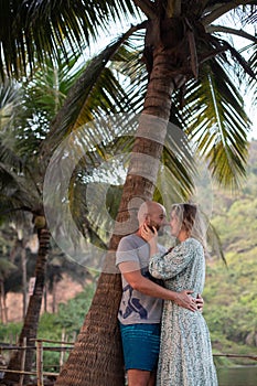 Happy couple look at each other and embrace under palm tree while relaxing in tropical paradise. Love and happiness.