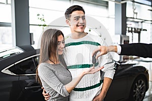 Happy couple look at the hand of a salesman while receiving car keys