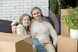 Happy couple looking at camera sitting on sofa, moving day