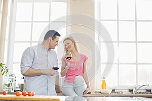 Happy couple looking at each other while drinking red wine in kitchen