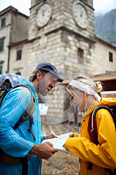 Happy couple looking at map for directions. Young man and woman on summer holiday in city, wearing raincoats. Travel, togetherness