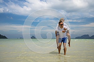 Happy couple in love on beach summer vacations. Joyful girl piggybacking on young boyfriend having fun