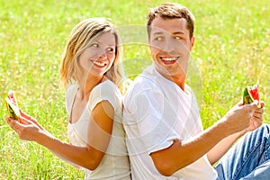 Happy couple in love eating watermelon outdoors in summer park