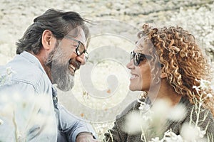 Happy couple in love enjoy spring and summer outdoor leisure activity sitting in the meadow with white blossom flowers around.