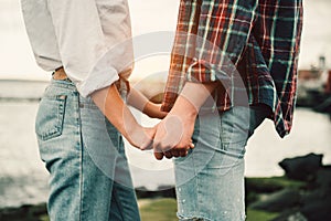 Happy couple in love holding hands at sunset time on the ocean wearing casual jeans outfit