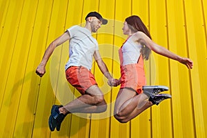 Happy couple in love jumping against yellow wall. Young hipsters