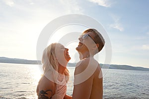 Happy couple in love laughing at the beach against sun