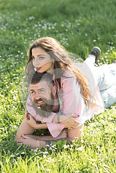 Happy couple in love lying on flowery meadow holding tiny white flowers in their mouths. Bearded man and his pretty