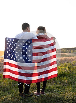 happy couple in love, a man and a woman, hold an American flag behind their backs, illuminated by sunlight