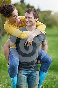 Happy couple, love and piggyback in nature for connection, trust and marriage in garden for holiday. Man, woman and fun