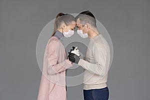 Happy couple in love in repsiratory masks and gloves hugging each other isolated on grey