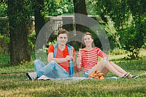 Happy couple in love resting in the park on the meadow. A couple of young people are sitting on a bed in a park in the summer and