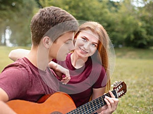 Happy couple in love on a romantic date at the park on a picnic. Playing on a guitar and having fun outdoors