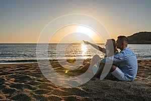 Happy couple in love, is seating on the beach during sunset or sunrise. Summer vacations