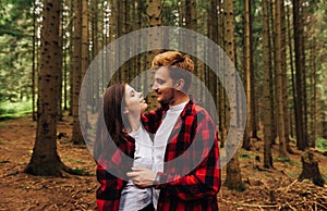 Happy couple in love standing in the arms in the woods and looking at each other in love  man and woman wearing red shirts. Photo
