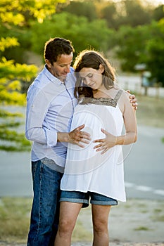 Happy couple in love together in park landscape on sunset with woman pregnant belly and man