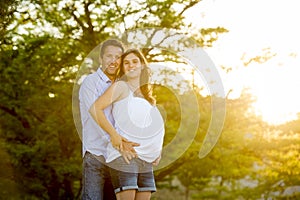 Happy couple in love together in park landscape on sunset with woman pregnant belly and man